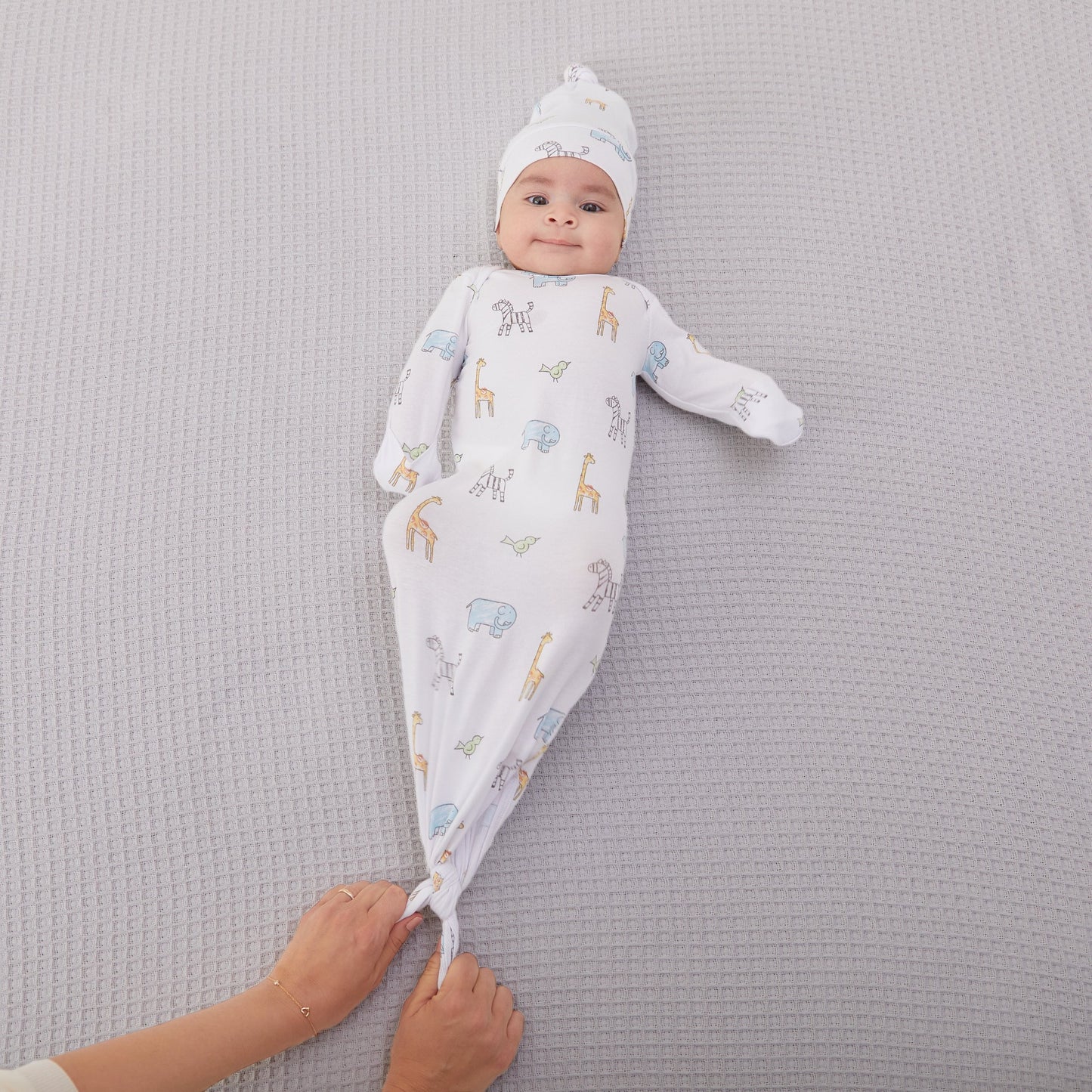 Kūdikis aprengtas balto smėlinuko ir kepurėlės komplektu su gyvūnėliais: žirafomis, drambliukais, zebriukais ir paukščiukais